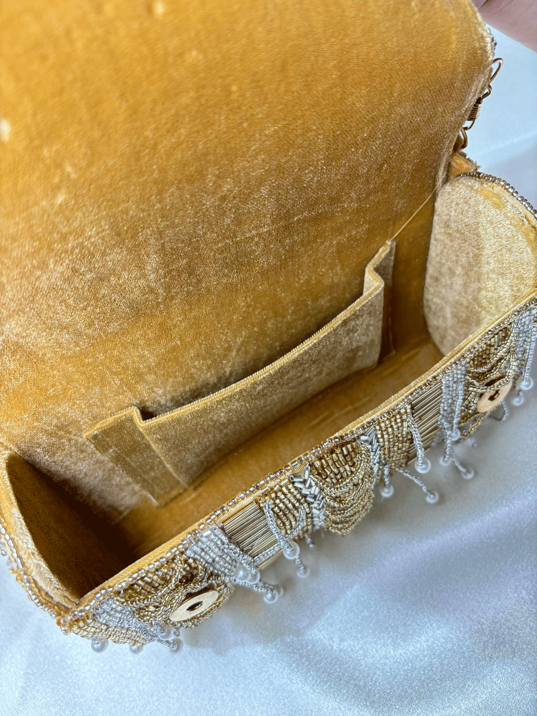 Gold beaded clutch bag with pearl accents on a neutral background